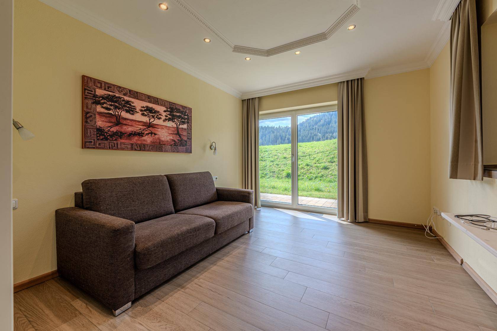 Helles Wohnzimmer mit bequemer Couch, Holzboden und weitem Blick auf die grüne Landschaft.