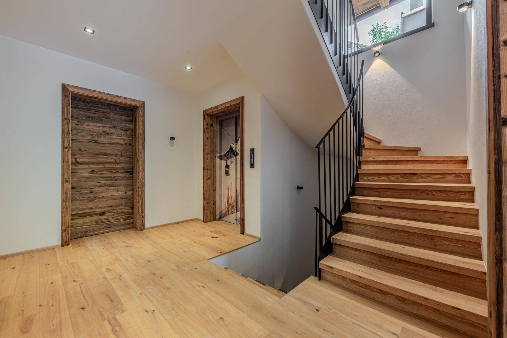 Heller Flur mit Holztreppe, Holzboden und rustikalen Holztüren.