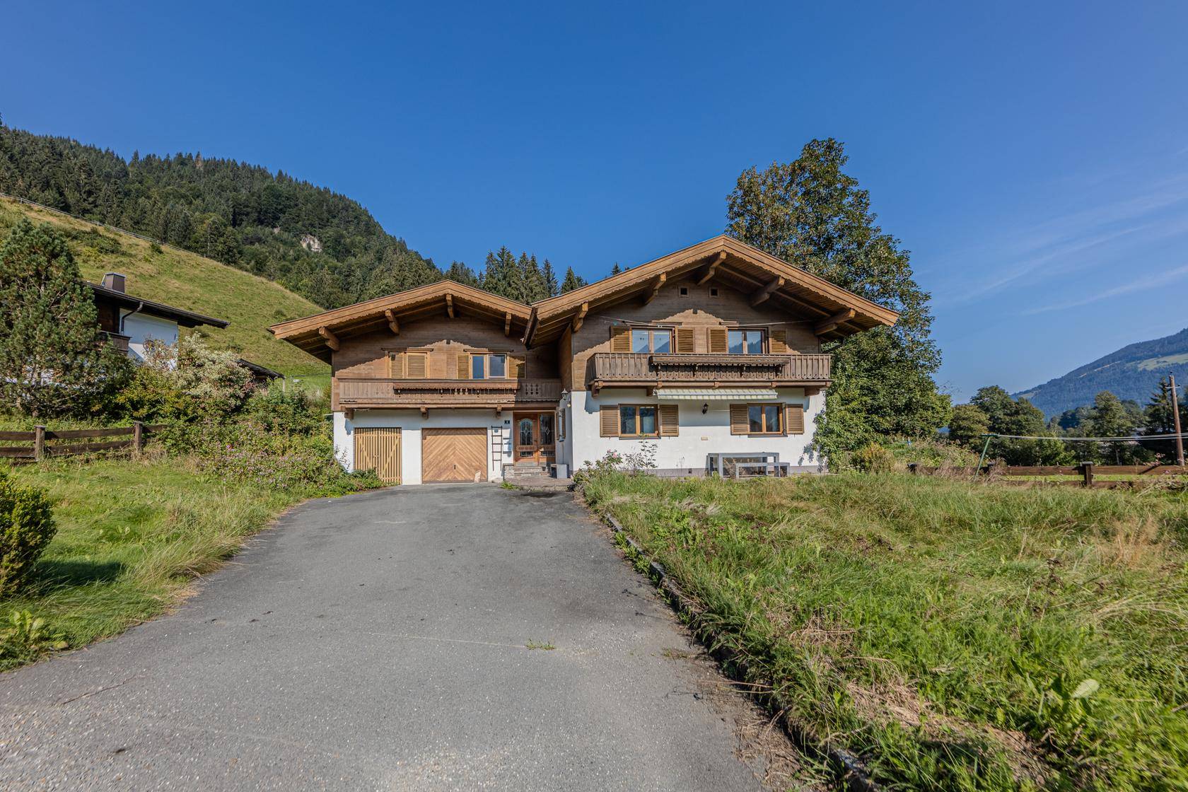 Traditionelles Landhaus mit Holzfassade, Balkonen und Garagenzufahrt in ländlicher Umgebung.