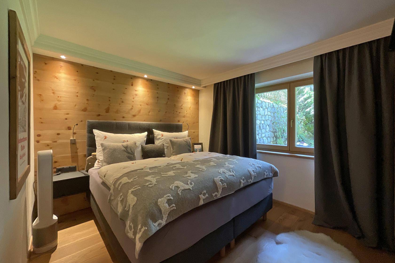 Gemütliches Schlafzimmer mit Holzwand, Doppelbett und Blick ins Grüne.