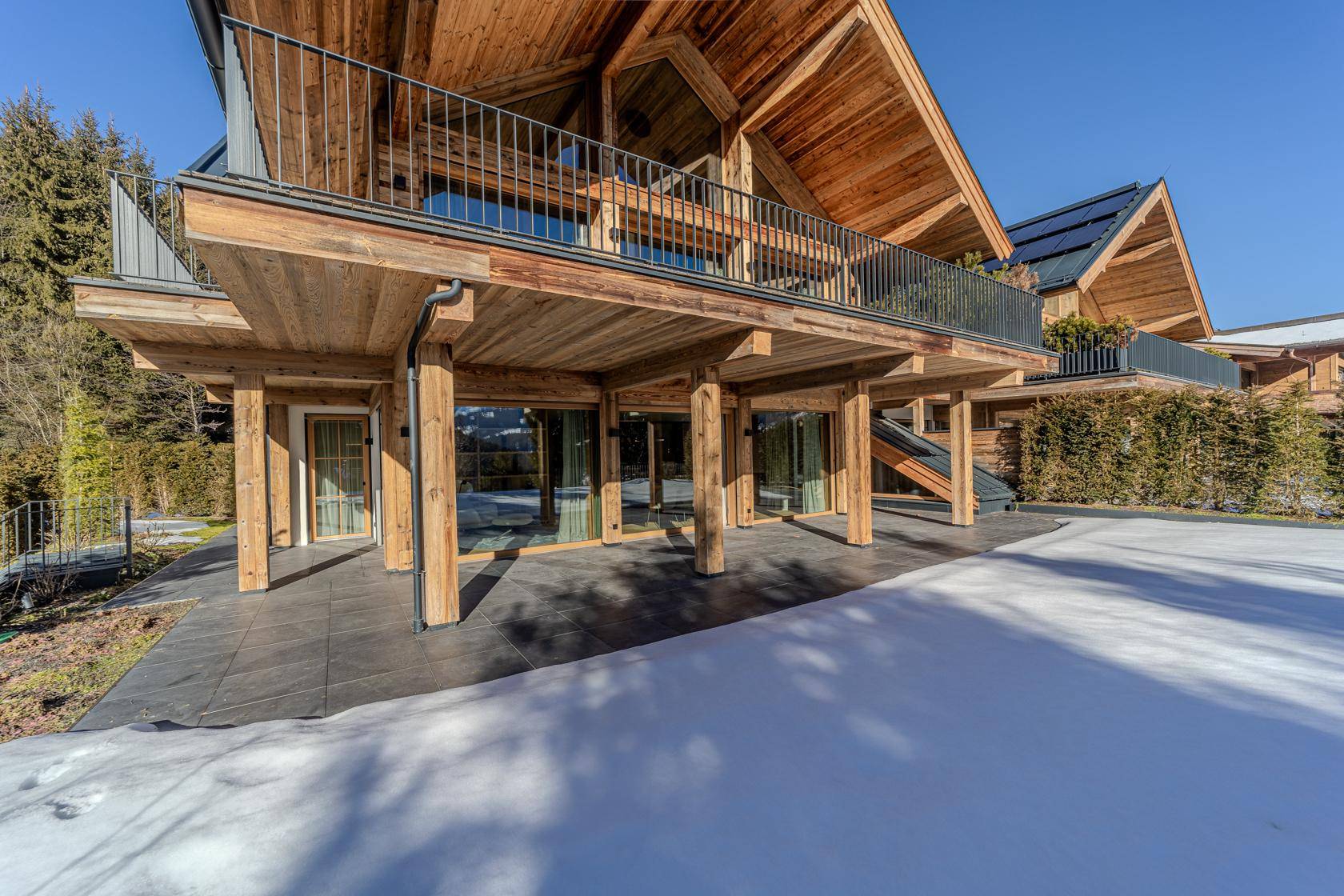 Moderne Holzarchitektur mit großer Terrasse und Blick auf die verschneite Berglandschaft.