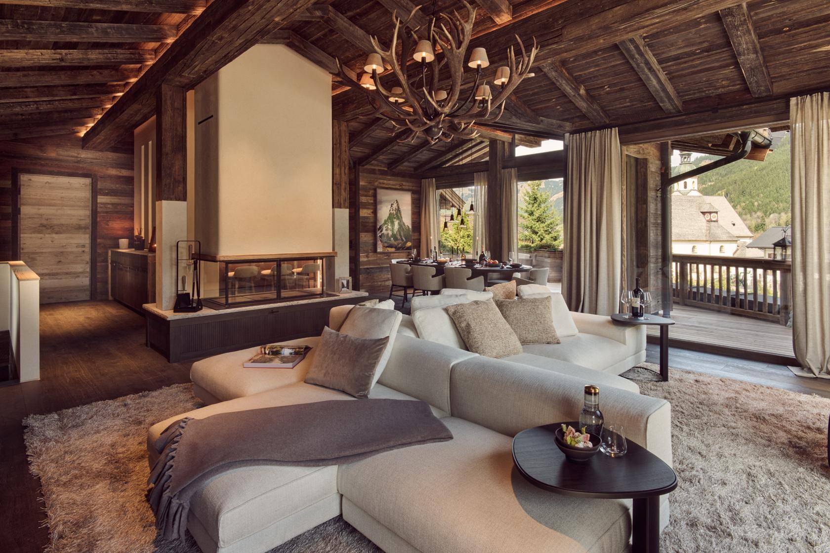 Luxuriöses Wohnzimmer im Chalet-Stil mit Kamin, Geweihleuchter und Zugang zum Balkon.