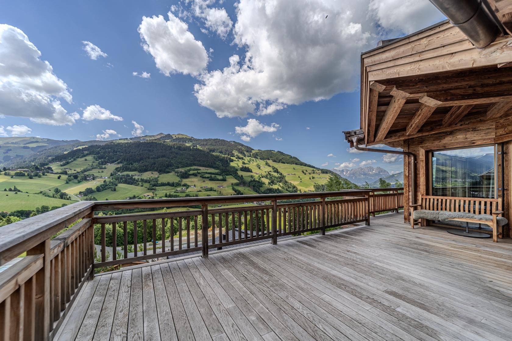 Weitläufige Holzterrasse mit Panoramablick auf die umliegende Berglandschaft und viel Sonnenschein.