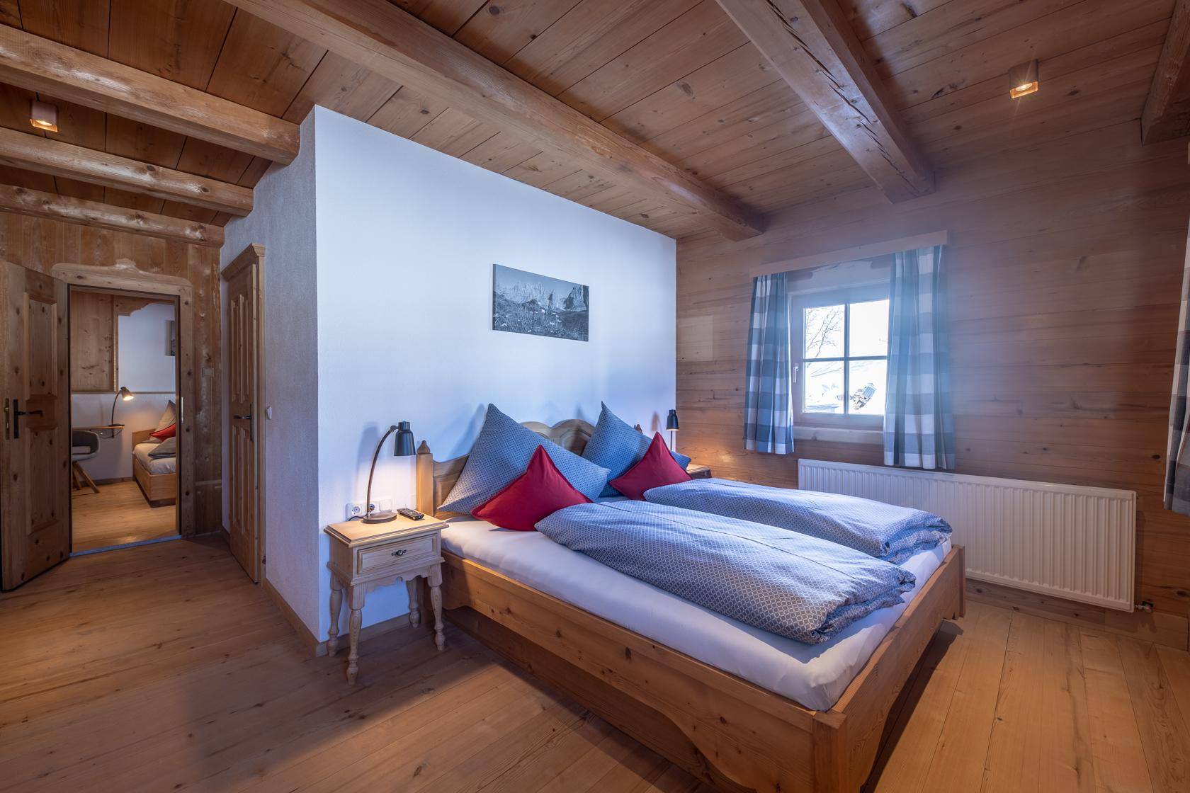 Gemütliches Schlafzimmer mit Holzboden, Holzbalkendecke und traditionellem Doppelbett.