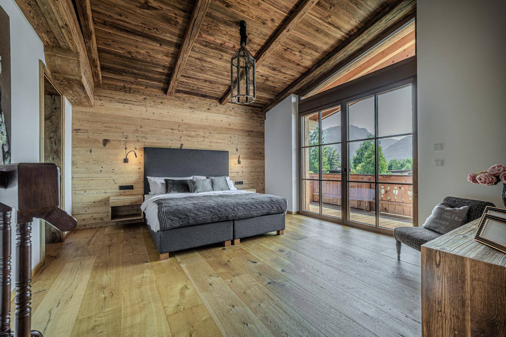 Schlafzimmer mit hohen Holzbalkendecken, Holzwänden und Balkonzugang mit herrlichem Bergblick.