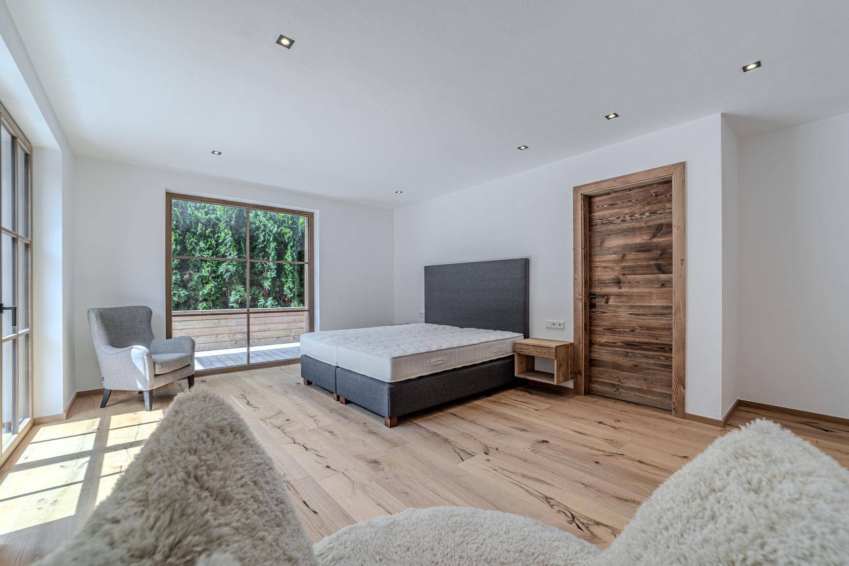 Helles Schlafzimmer mit Doppelbett, Holzboden und großen Fenstern mit Blick ins Grüne.