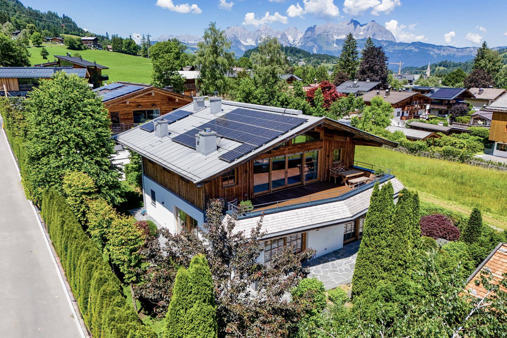 Luftaufnahme eines modernen Hauses mit Solaranlage und Bergblick in grüner Umgebung.