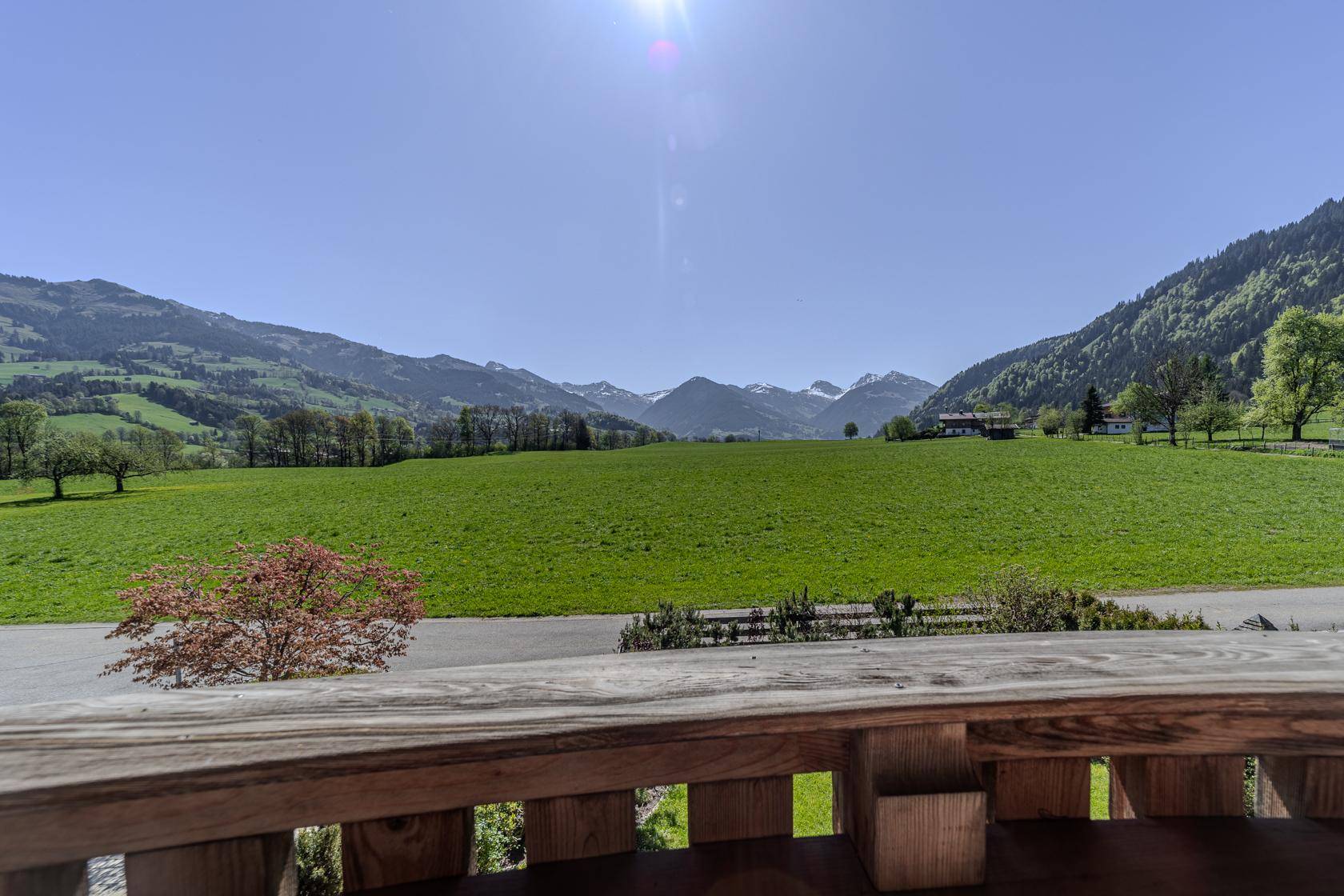 Weitläufiger Panoramablick über grüne Täler und schneebedeckte Berggipfel unter strahlend blauem Himmel.
