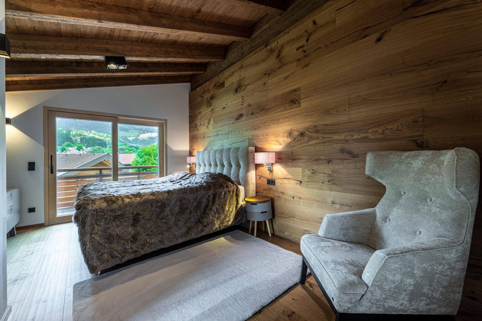 Schlafzimmer mit Holzwand, großem Bett und Zugang zu einem kleinen Balkon.