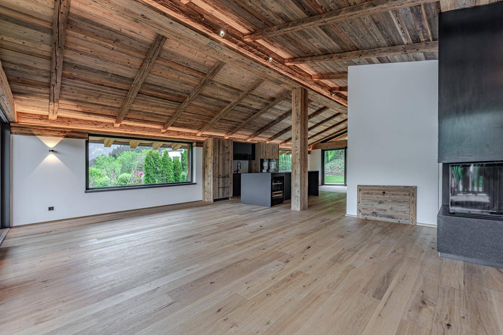 Geräumiges Wohnzimmer mit modernem Kamin, Holzbalkendecke und großen Fenstern.
