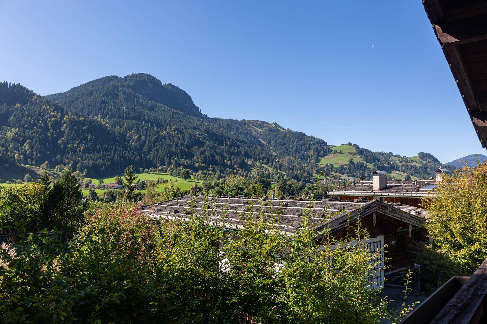 Weitläufiger Blick über bewaldete Hügel und Dächer von Häusern in alpiner Landschaft.