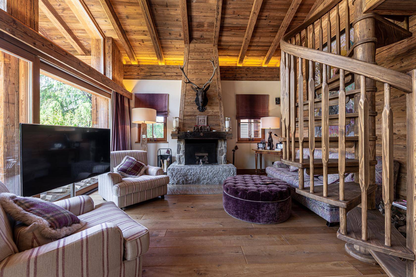 Rustikales Wohnzimmer mit Kamin, Holzvertäfelung, Wendeltreppe und gemütlichen Sitzgelegenheiten.