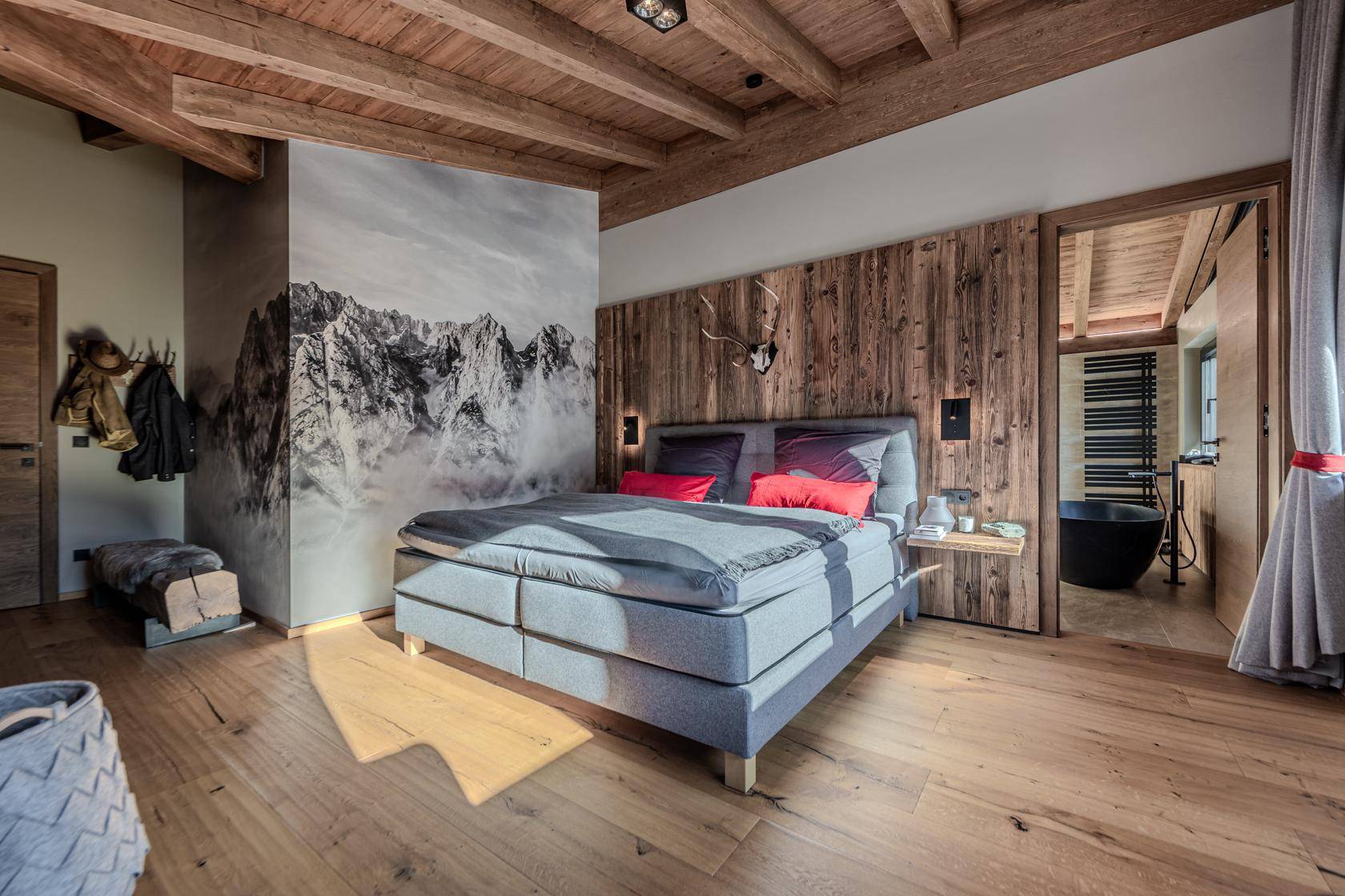 Schlafzimmer im Chalet-Stil mit Holzwand, Bergbild-Wandtapete und direktem Zugang zum Badezimmer.