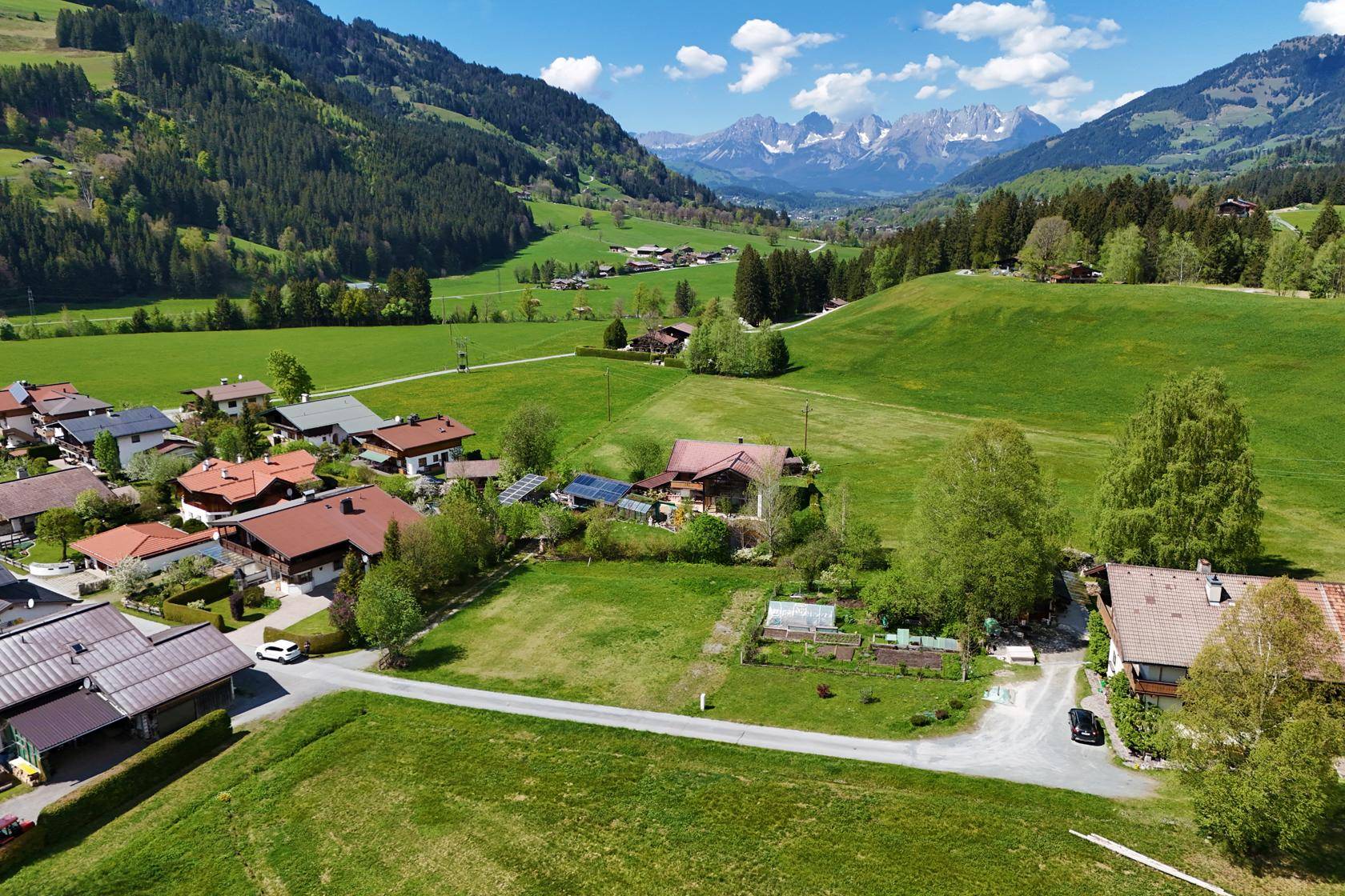 Weitläufige Luftaufnahme eines Dorfes in den Bergen mit traditionellen Häusern und viel Grün.