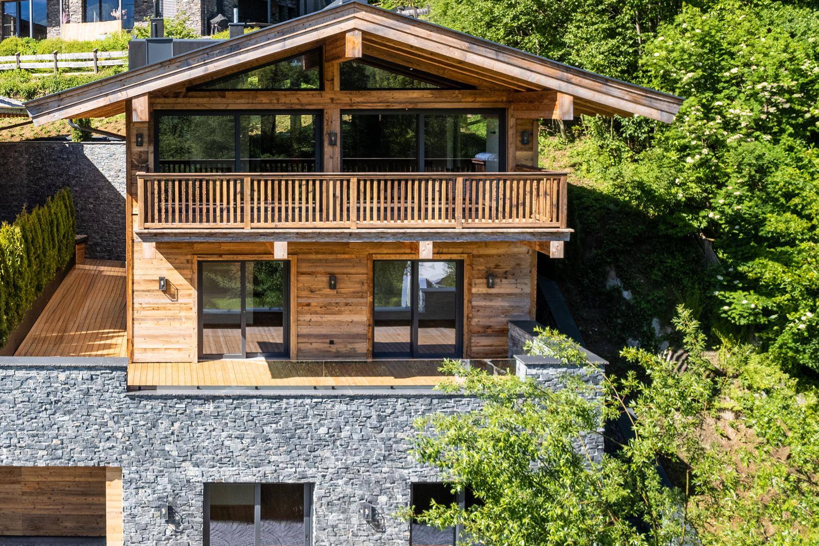 Ansicht eines luxuriösen Chalets mit Holzfassade, Balkonen und Steinelementen in den Bergen.