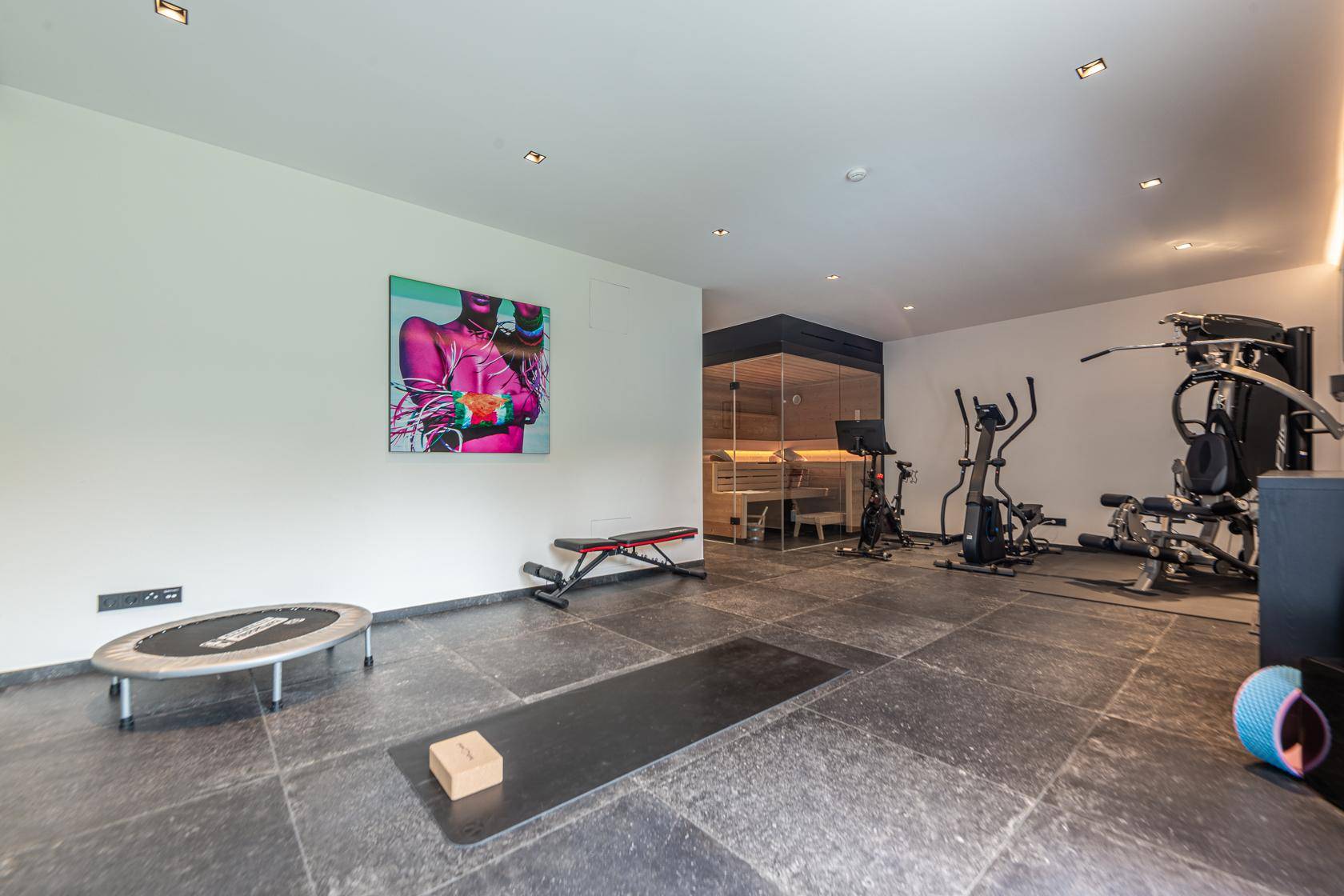 Geräumiger Fitnessraum mit verschiedenen Trainingsgeräten und integrierter Sauna.