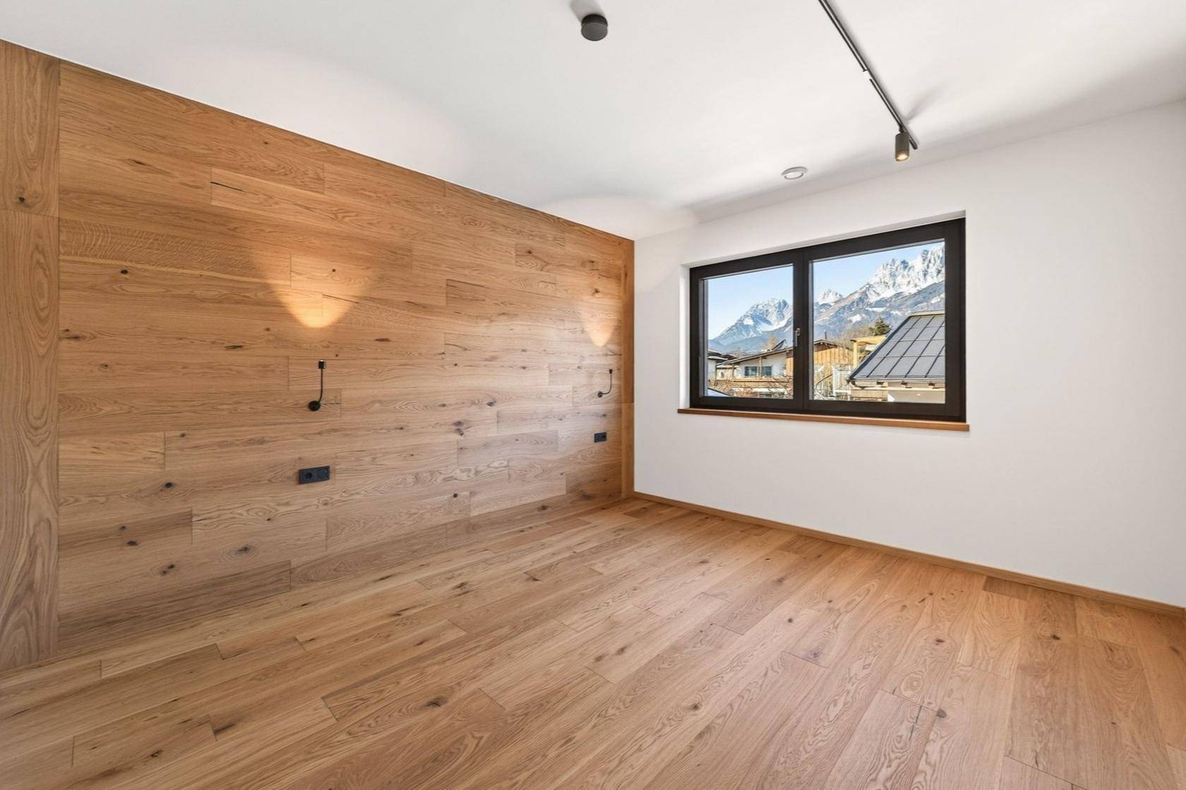 Helles Schlafzimmer mit Holzwandverkleidung, Holzboden und malerischem Bergblick.