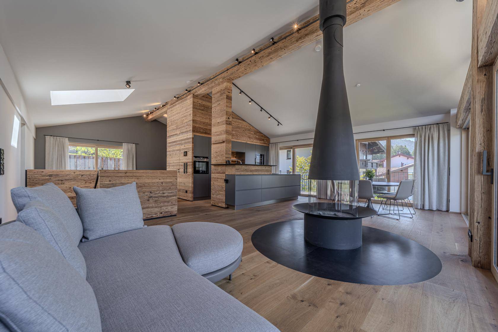 Offener Wohnbereich mit gemütlichem Sofa, Kamin und Blick auf die moderne Küche.