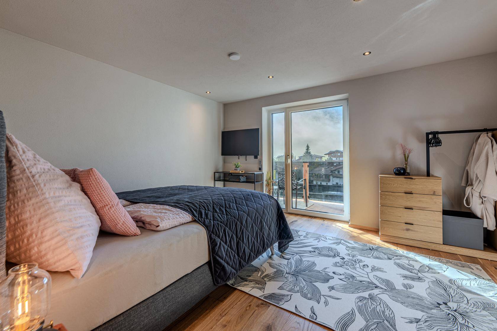 Helles Schlafzimmer mit Holzboden, Balkonzugang und Blick auf die umliegende Landschaft.