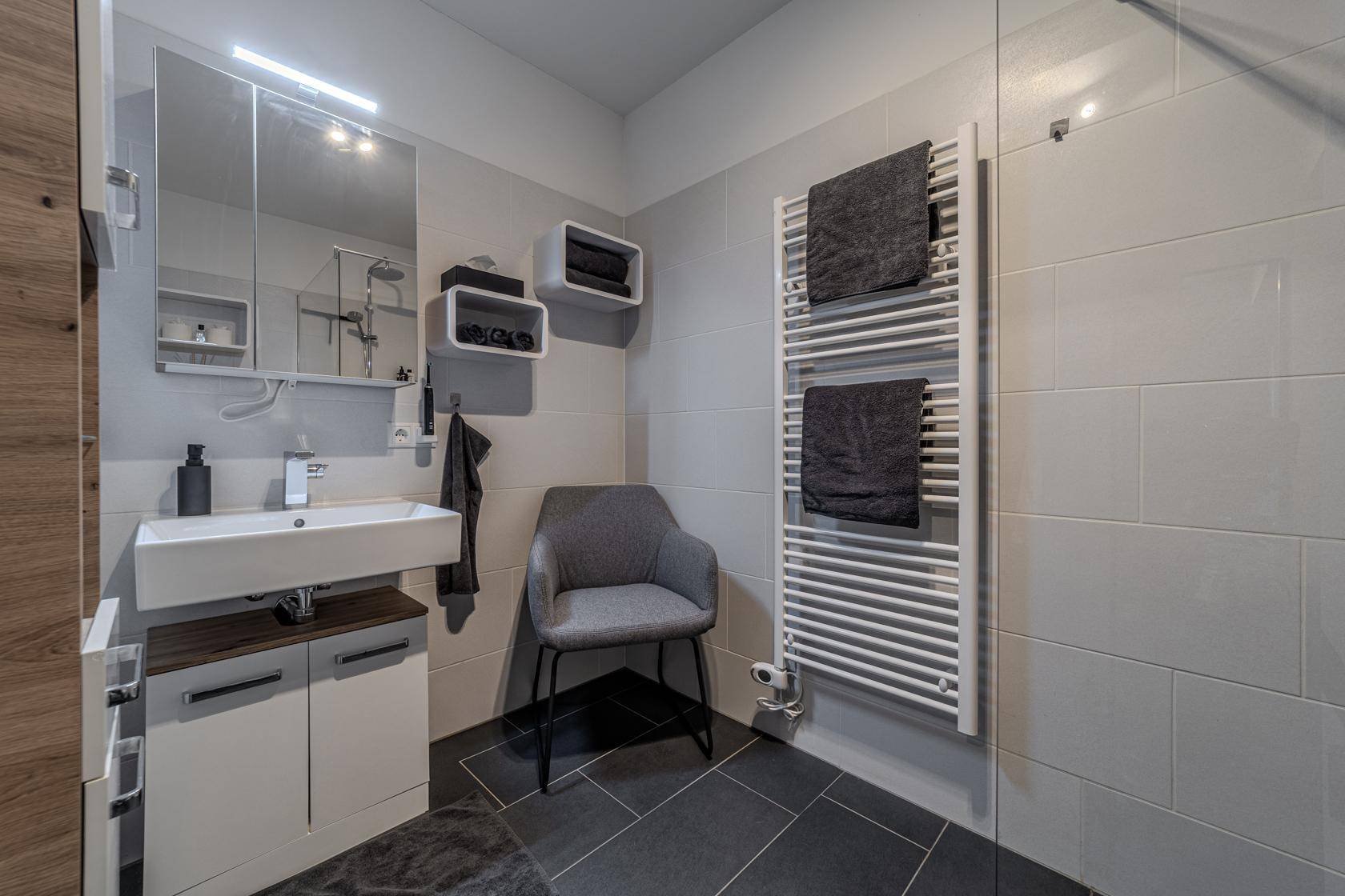 Modernes Badezimmer mit grauen Fliesen, Waschtisch und beheiztem Handtuchhalter.