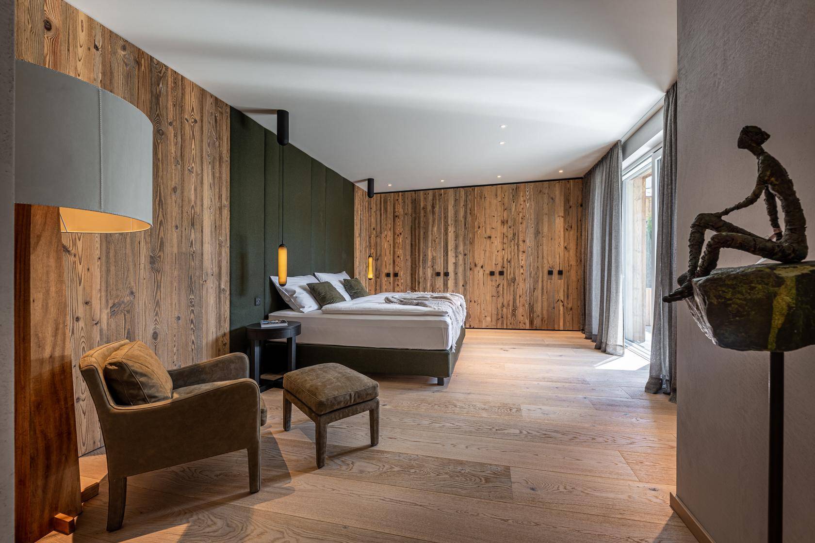 Helles Schlafzimmer mit Holzwänden, großem Fenster und Zugang zu einem Außenbereich.