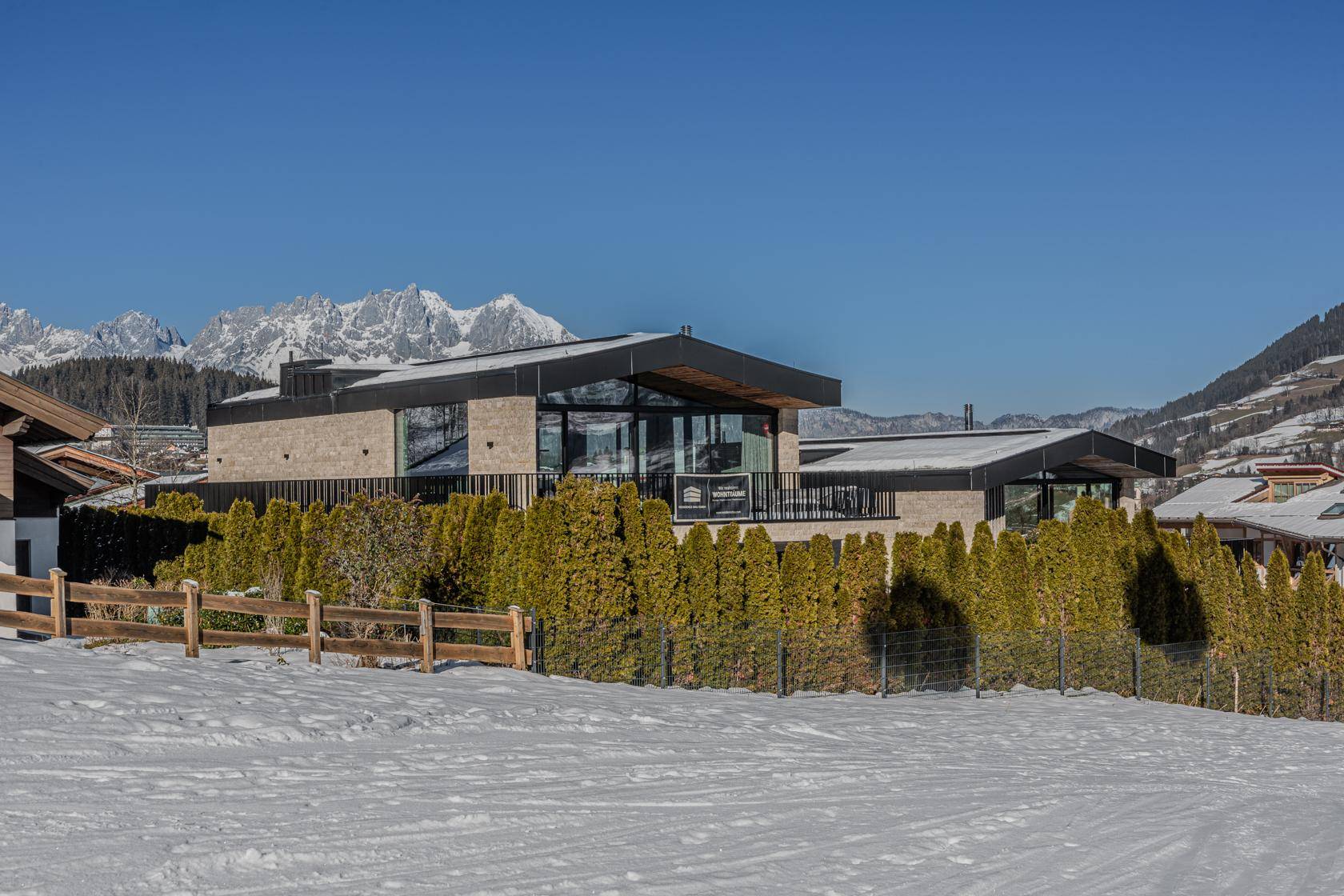 Moderne Villa mit Flachdach und großen Glasfronten, umgeben von Schnee und Bergen.