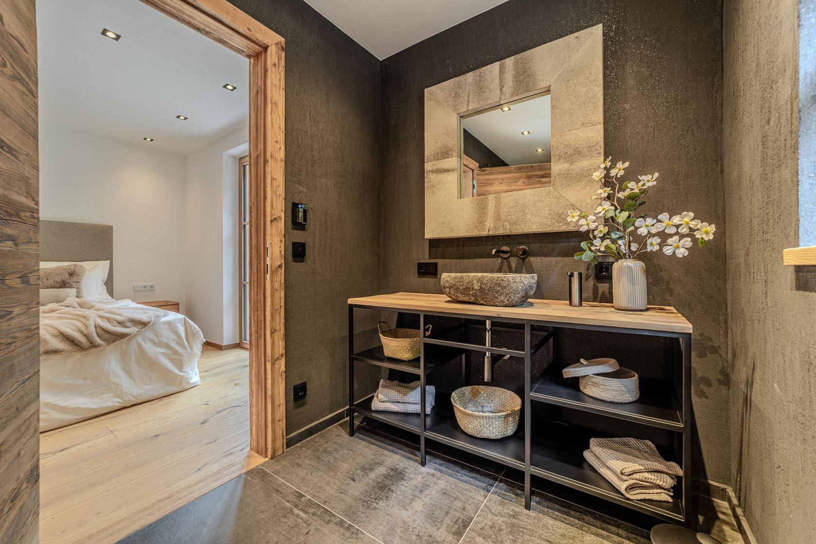 Modernes Badezimmer mit dunklen Fliesen, Holzwaschtisch und direktem Zugang zum Schlafzimmer.