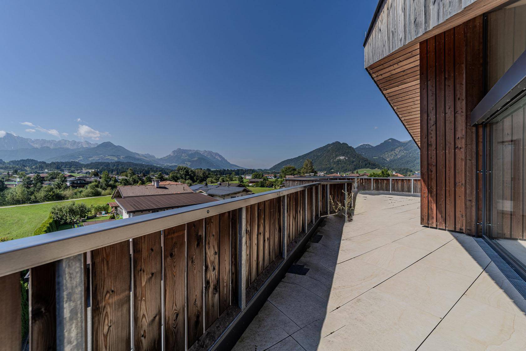Weitläufige Terrasse mit Holzgeländer und Panoramablick auf die umliegende Berglandschaft und das Tal.