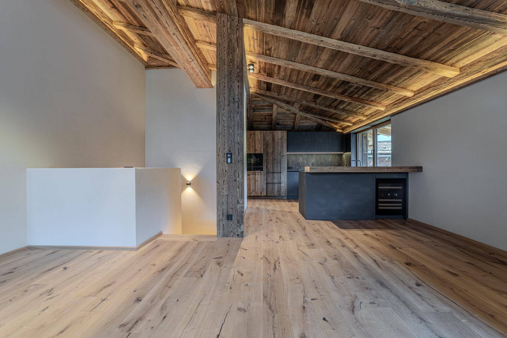 Heller offener Wohnbereich mit rustikaler Holzbalkendecke und integrierter Küche in modernem Design.