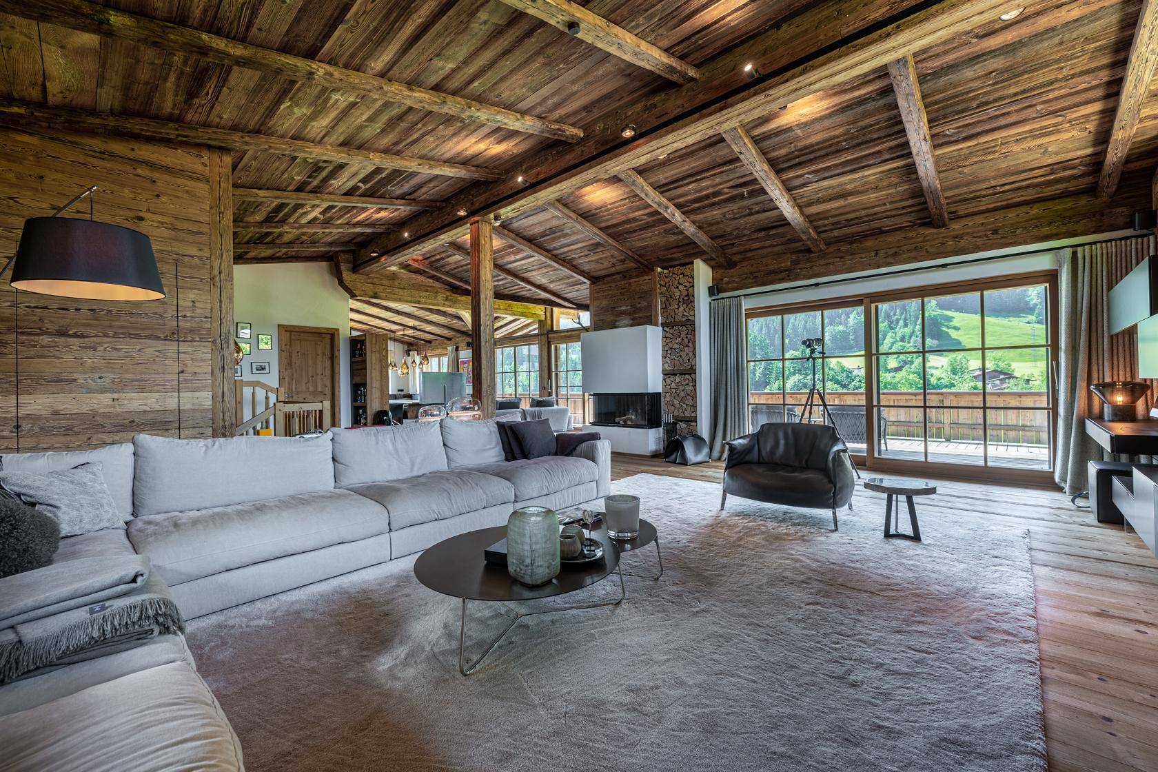 Gemütliches Wohnzimmer im Chalet-Stil mit Holzbalkendecke, Kamin und Zugang zur Terrasse.