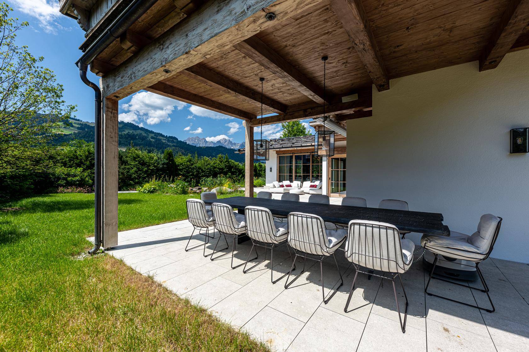 Überdachte Terrasse mit großem Esstisch und Stühlen, ideal für Mahlzeiten im Freien mit Bergblick.