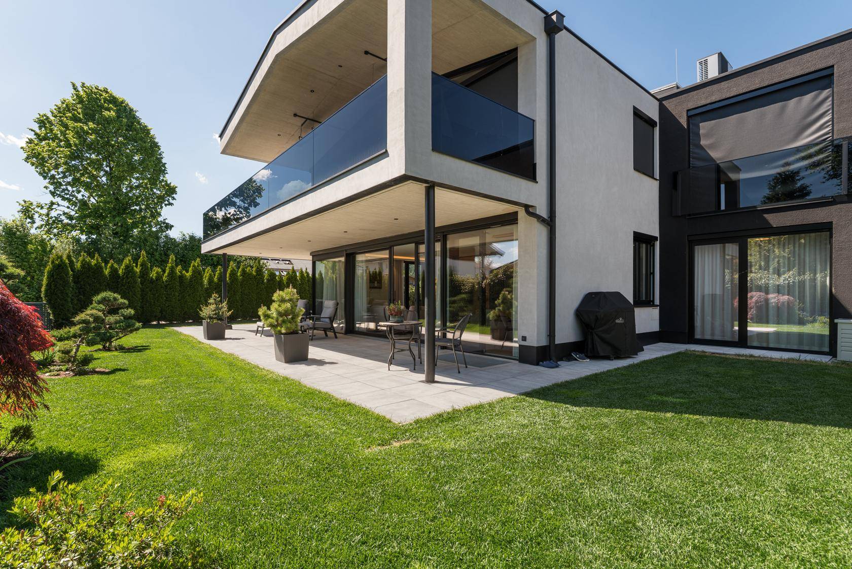 Moderne Villa mit großer Terrasse, gepflegtem Rasen und Grillbereich im Freien.