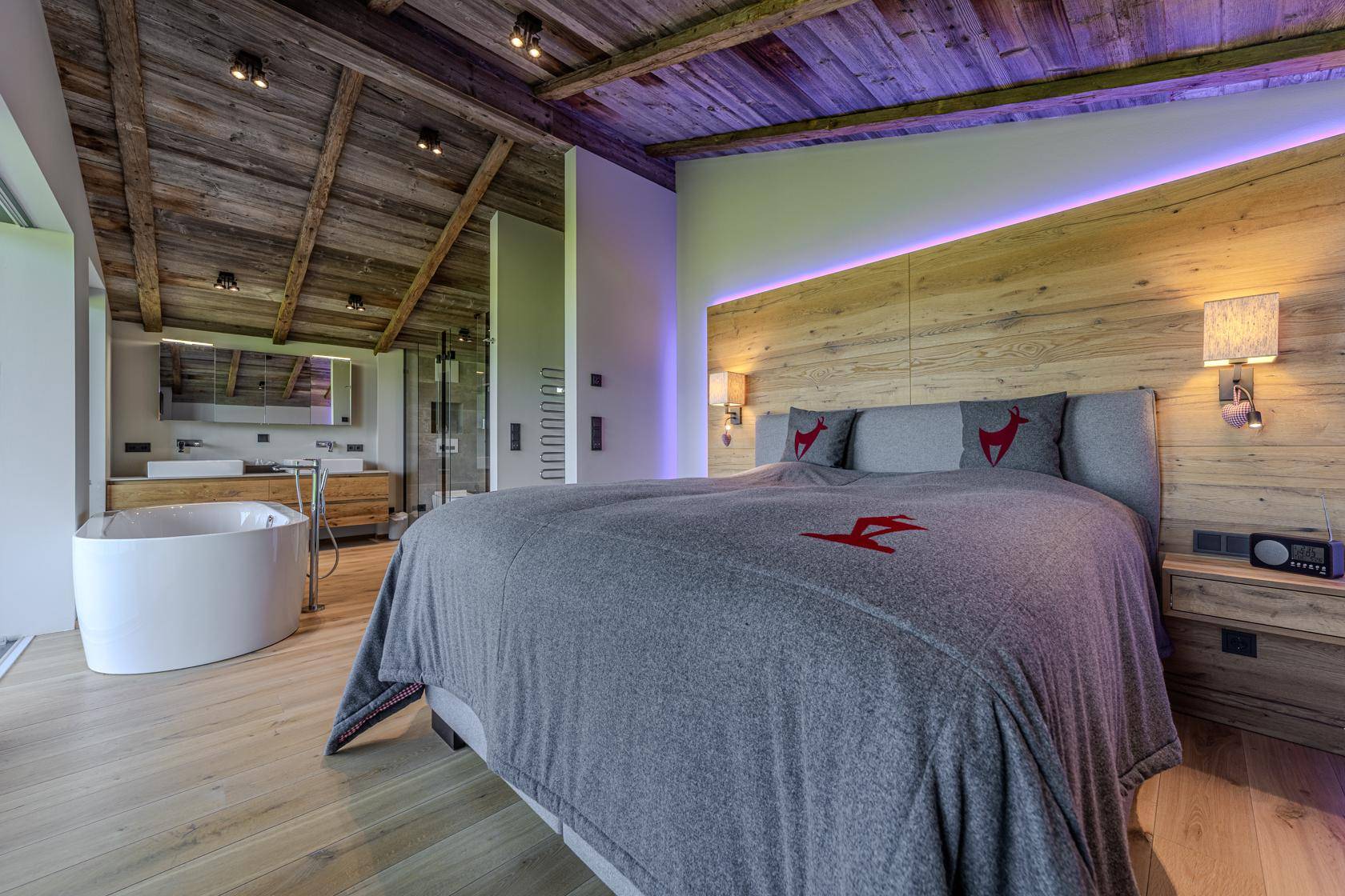Schlafzimmer mit Holzakzentwand, indirekter Beleuchtung und offenem Übergang zum Badezimmer.