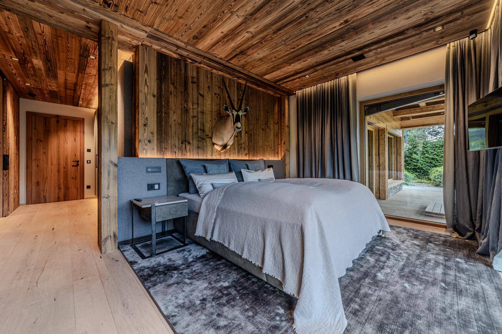 Gemütliches Schlafzimmer mit Holzbalkendecke, weichem Teppich und traditioneller Hirschgeweih-Dekoration.