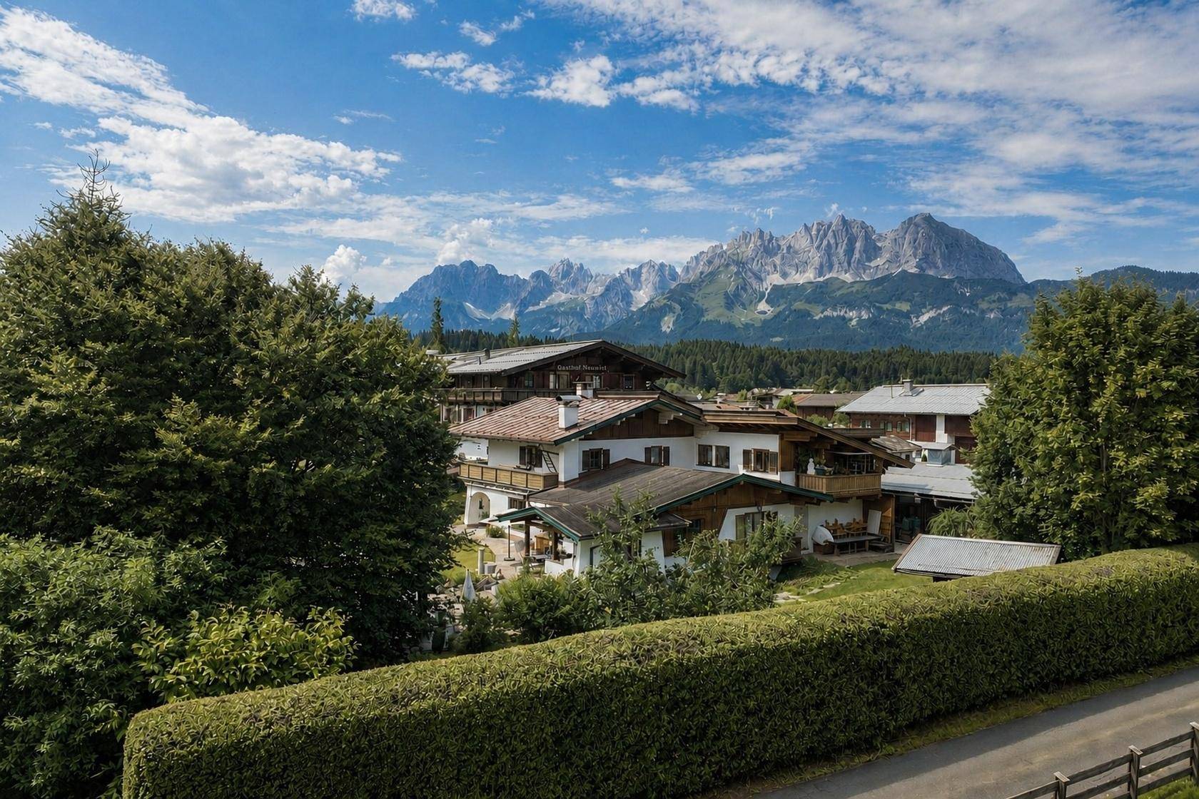 Ansicht von traditionellen Häusern mit Bergblick, umgeben von grünen Bäumen und einer Hecke.