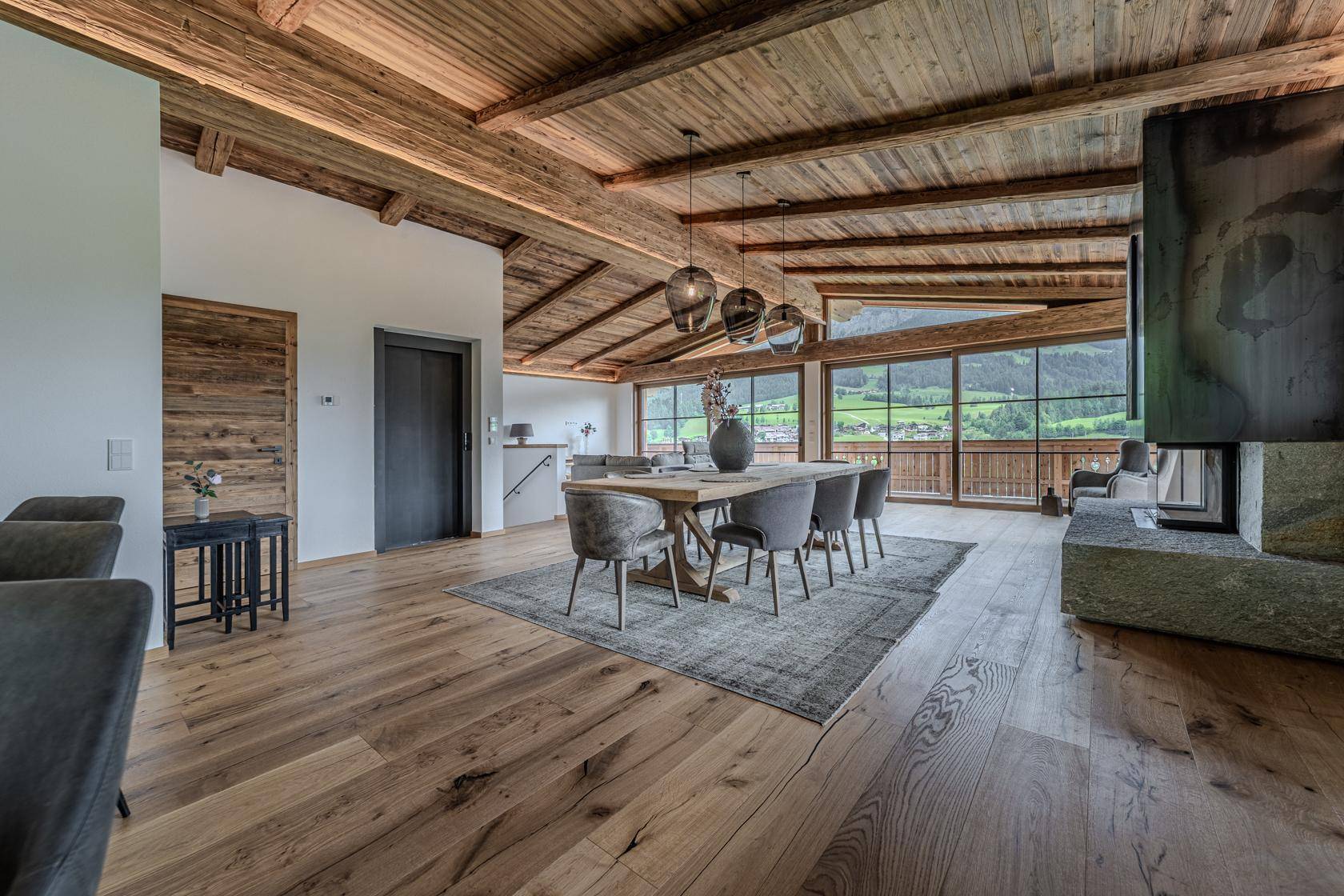 Heller Essbereich mit Holzbalkendecke, großem Tisch und Zugang zum Balkon mit Bergblick.
