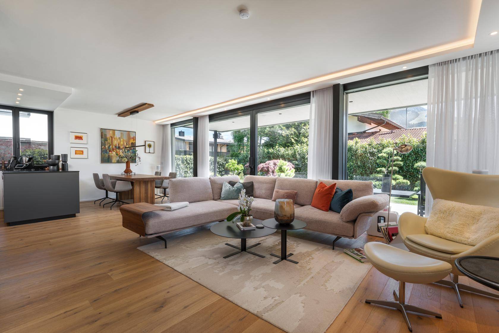 Moderner Wohnbereich mit beigem Sofa, Holzboden und Blick auf den grünen Garten.