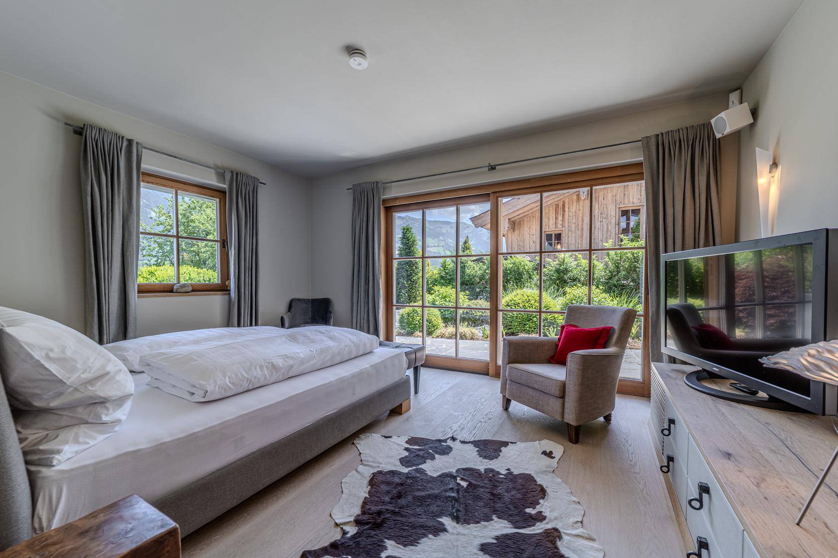 Helles Schlafzimmer mit Doppelbett, Fernseher und direktem Zugang zum Garten.