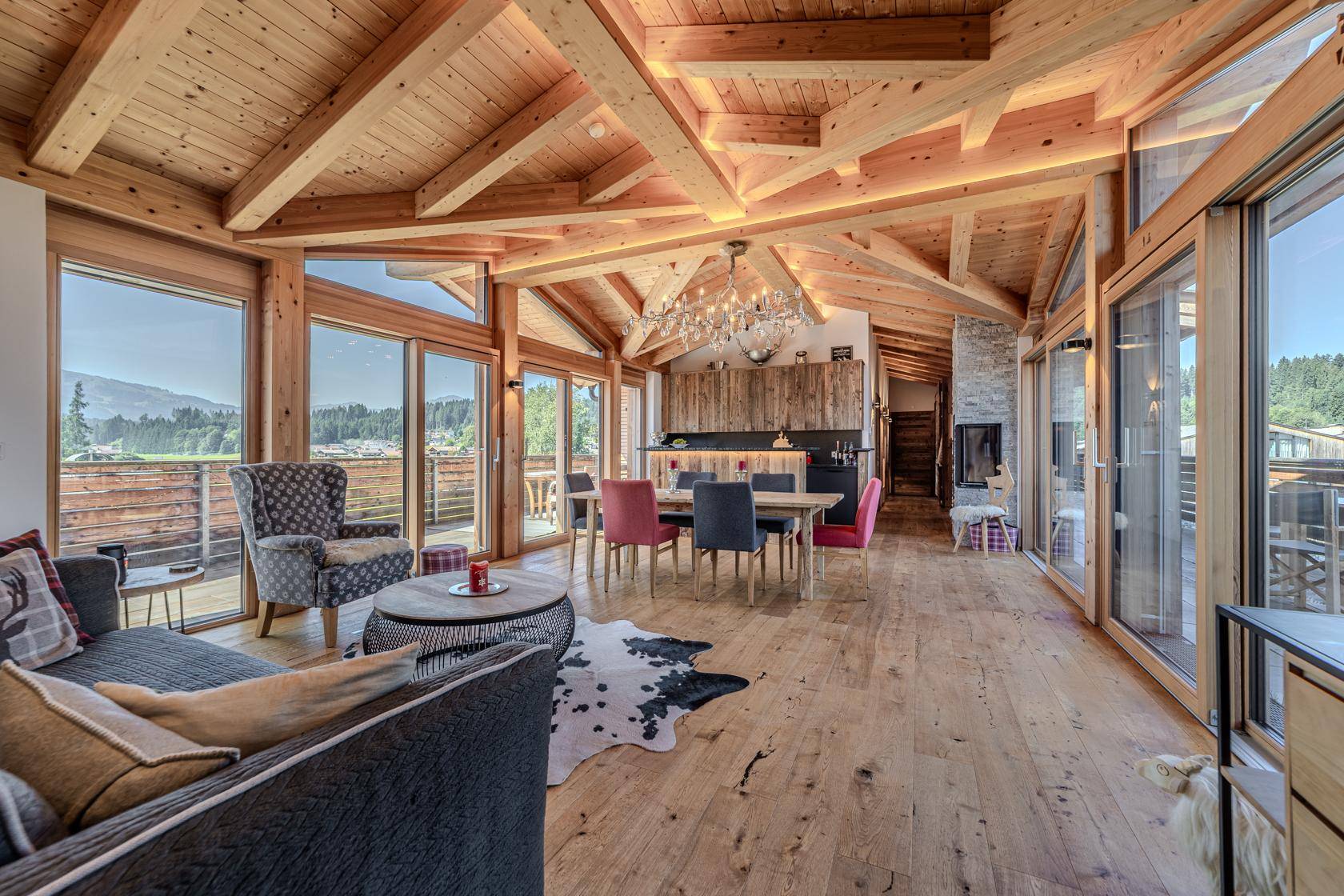 Heller offener Wohnbereich mit Holzbalken, integrierter Küche und Zugang zum Balkon.