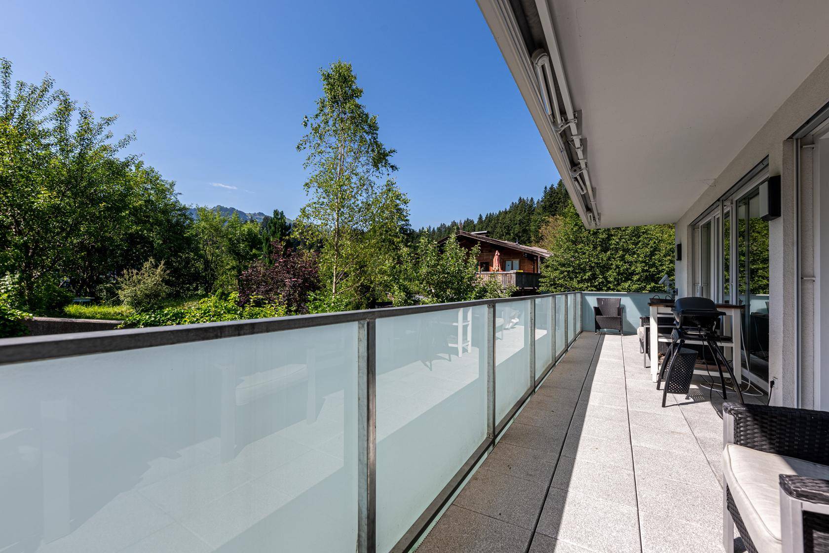 Langer Balkon mit Glasbrüstung, Sitzgelegenheiten und Blick ins Grüne.