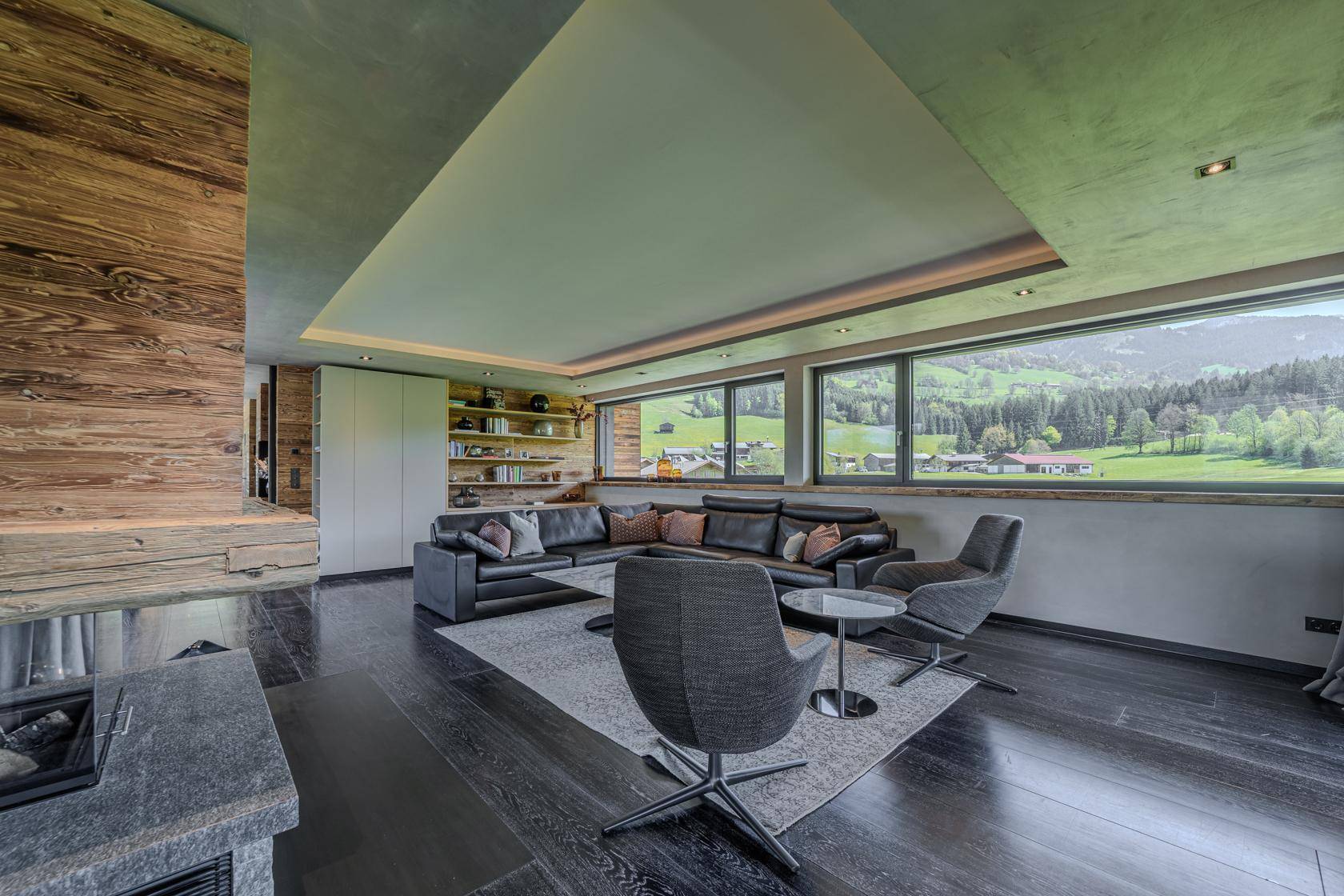 Helles Wohnzimmer mit dunklem Holzboden, großen Panoramafenstern und Blick auf die Natur.