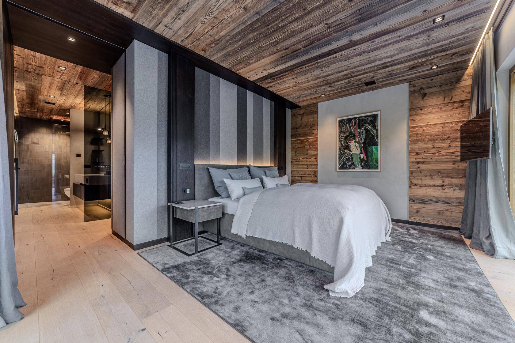 Modernes Schlafzimmer mit Holzbalkendecke, stilvoller Wandgestaltung und direktem Zugang zum Bad.