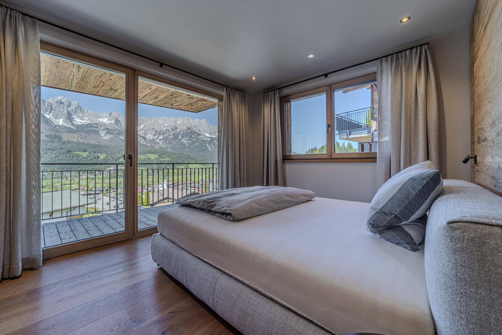 Schlafzimmer mit Holzboden, großem Fenster und direktem Zugang zum Balkon mit Bergblick.
