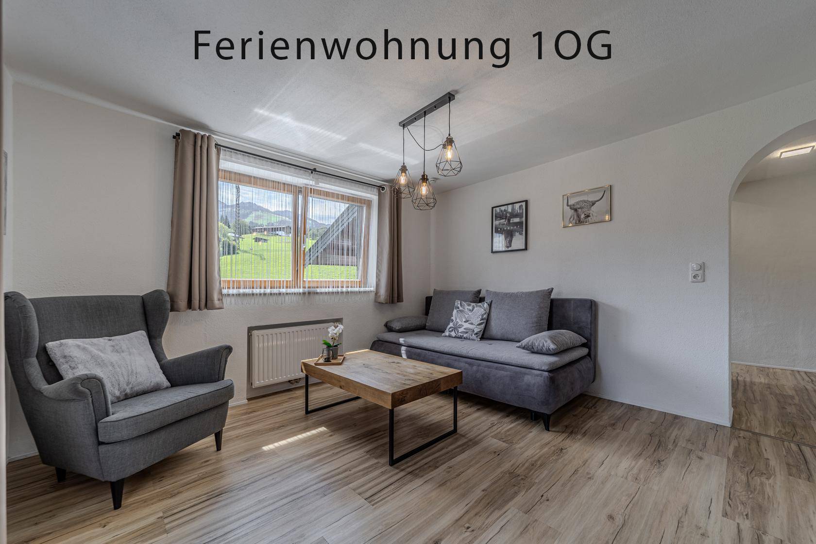 Helles Wohnzimmer mit Sofa, Sessel und Holzboden, mit Blick auf die grüne Landschaft.