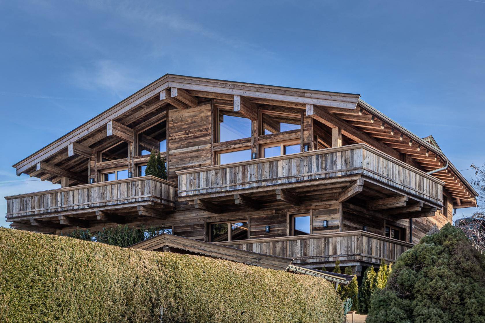 Charmantes Chalet-Gebäude aus Holz mit mehreren Balkonen und großen Fenstern, eingebettet in die Landschaft.