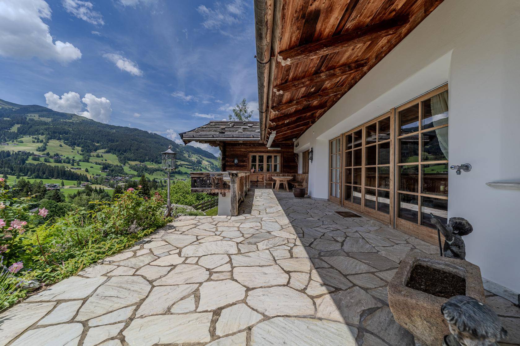 Sonniger Steinterrasse mit weitem Blick auf die grüne Berglandschaft und das charmante Landhaus.