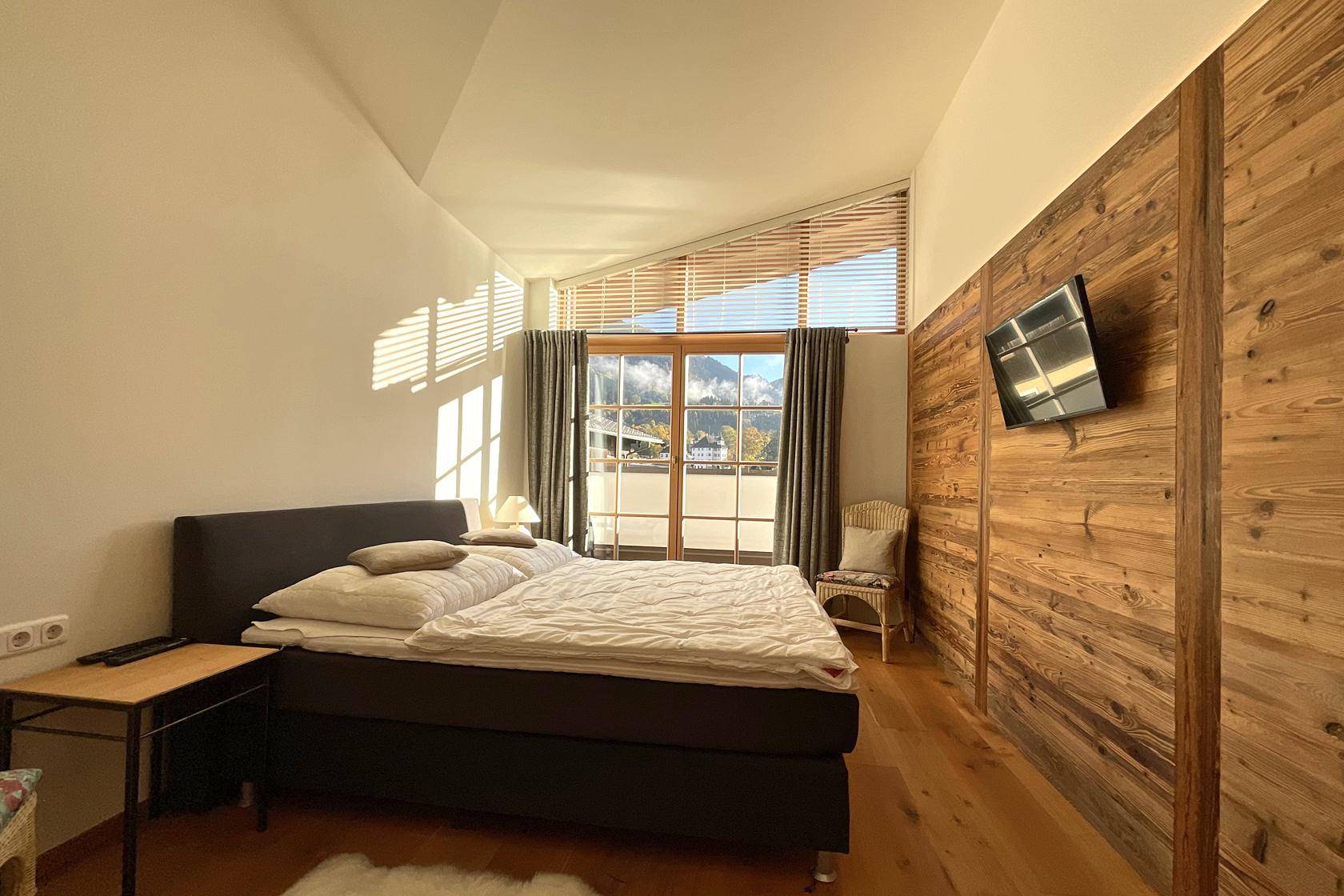 Schlafzimmer mit Doppelbett, Holzwand und großen Fenstern mit beeindruckendem Bergblick.