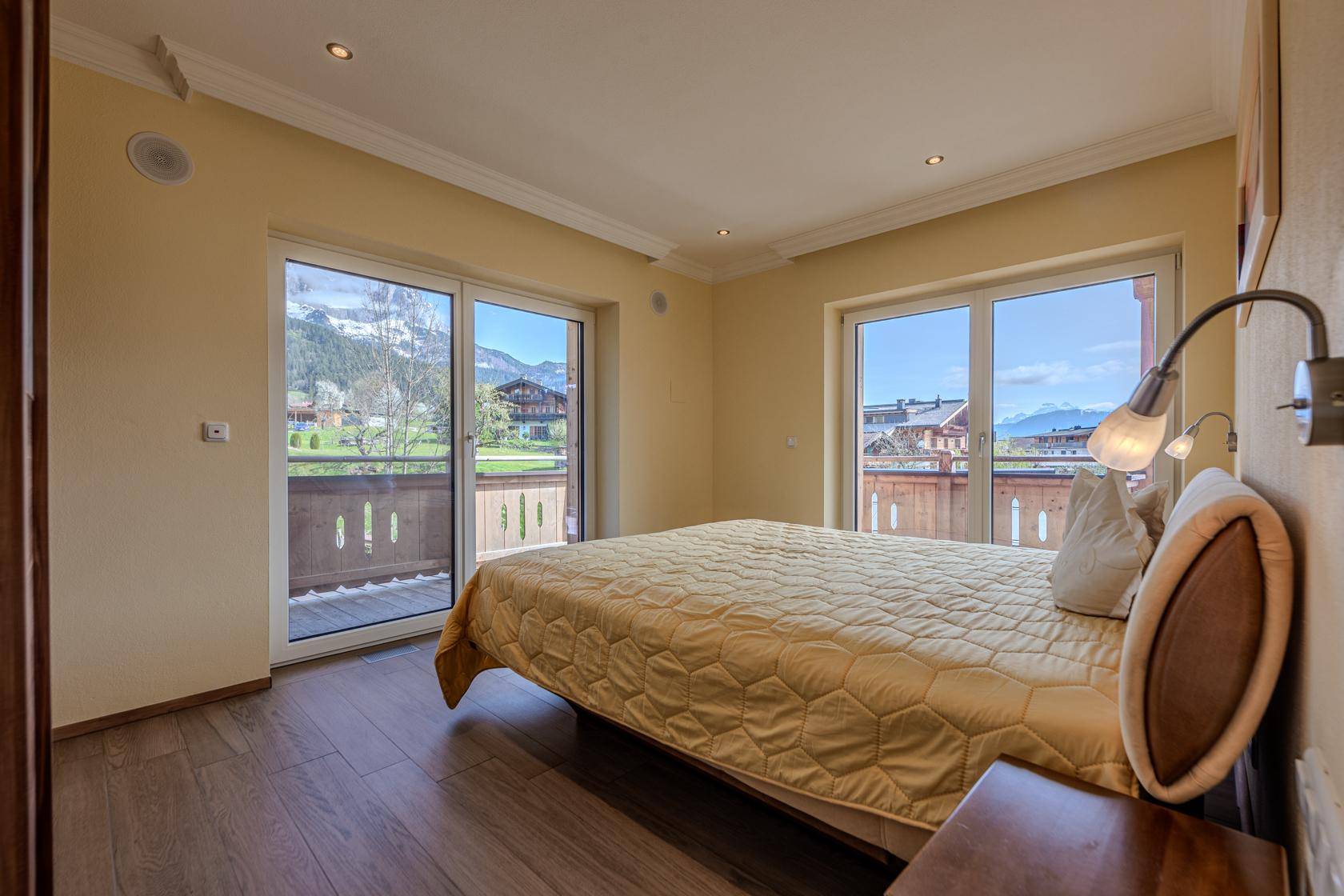 Gemütliches Schlafzimmer mit Doppelbett, Holzboden und direktem Zugang zum Balkon mit Bergblick.