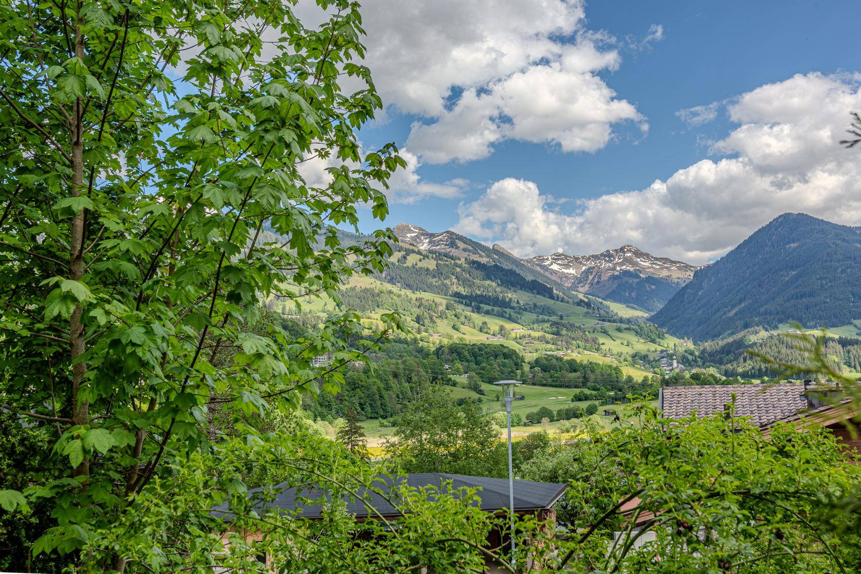 Weitläufiger Ausblick auf die alpine Landschaft mit bewaldeten Bergen und sonnigen Tälern.