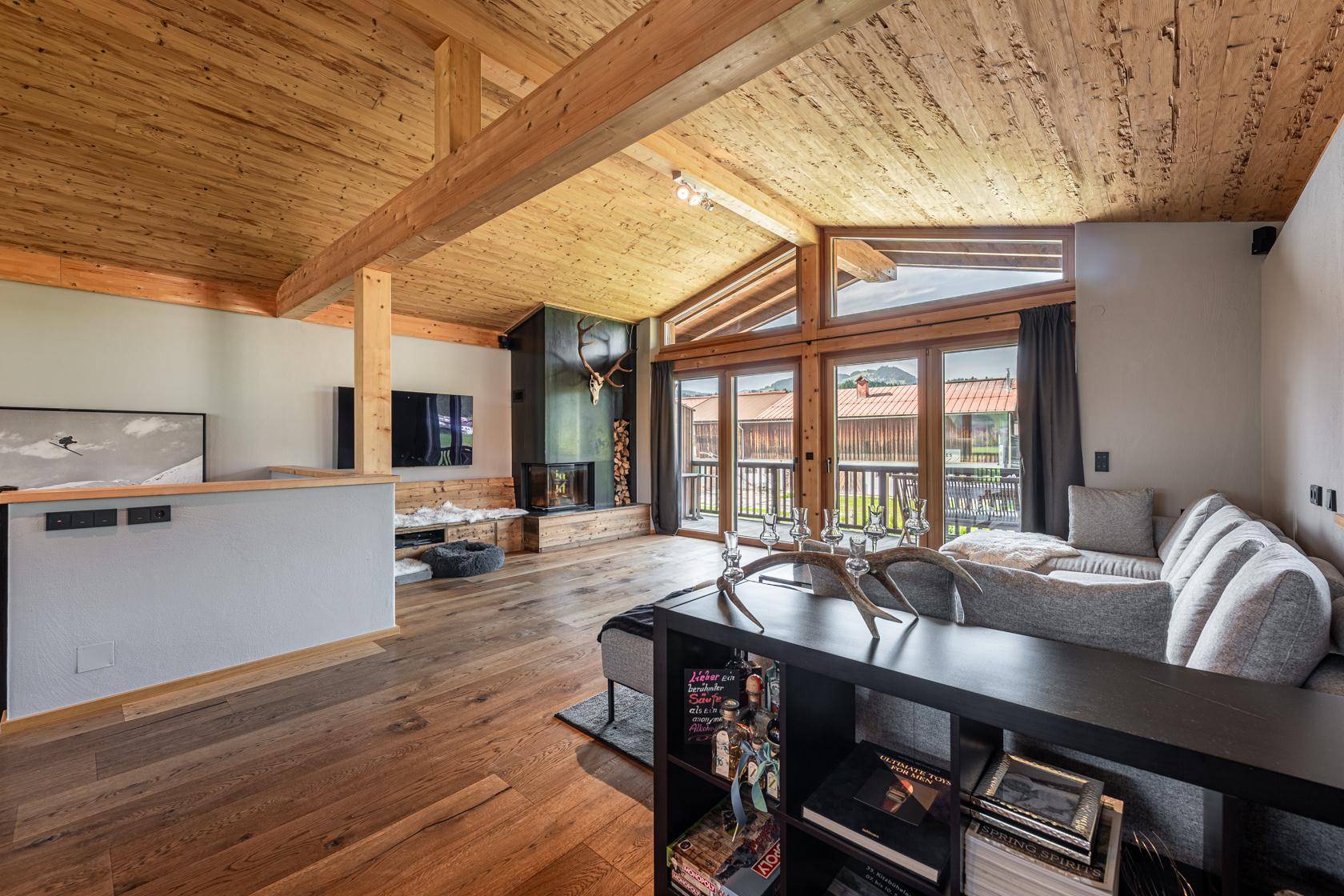 Gemütliches Wohnzimmer mit Kamin, großen Fenstern und Holzbalkendecke.